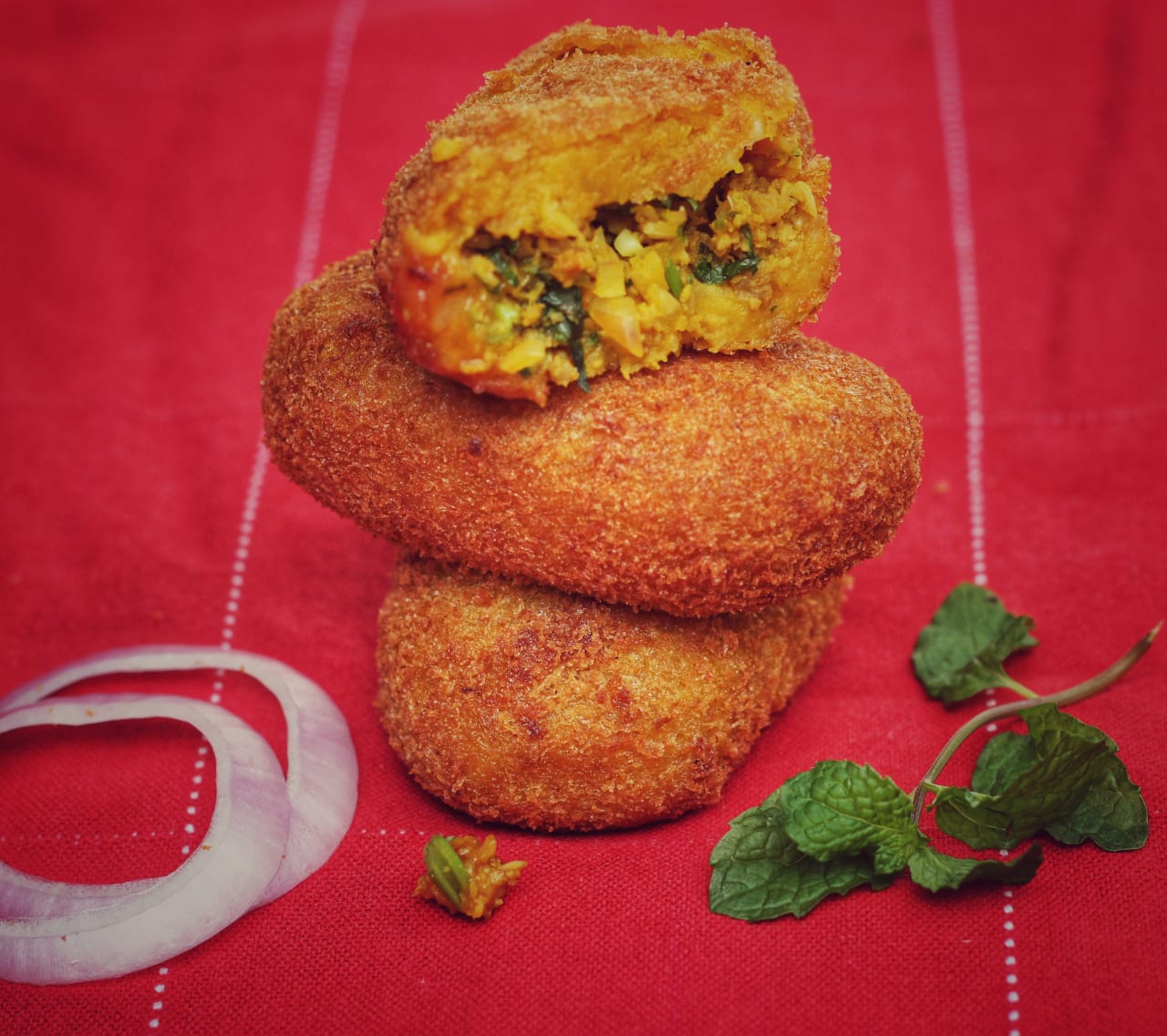 Stack of crumb fried cutlets with onion rings and mint
